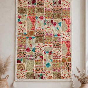 May include: A rectangular wall hanging featuring a patchwork design of various embroidered fabric squares. The textile displays a vibrant array of floral, paisley, and geometric patterns in shades of red, green, gold, and blue, finished with white tassels.