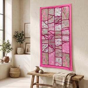 Pode incluir: Uma tapeçaria retangular com um design de patchwork de painéis de tecido rosa e prateado. O tecido é decorado com bordados intrincados, detalhes em fio metálico e pequenas lantejoulas refletoras dispostas em vários padrões geométricos.