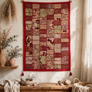 May include: A rectangular wall hanging featuring a patchwork design of deep red fabric squares. Each square is decorated with intricate gold-colored embroidery, metallic thread patterns, and floral motifs. The piece has a red border and two tassels.