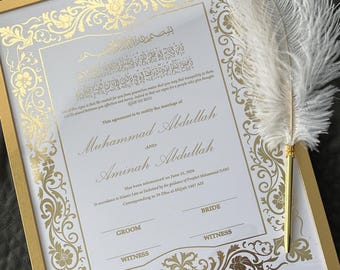 May include: A framed wedding certificate with gold floral accents and text in English and Arabic. The names Muhammad Abdullah and Aminah Abdullah are featured. A white feather quill pen rests on the frame.