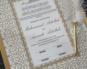 May include: A framed marriage certificate with gold accents and ornate border designs. The certificate includes Arabic script and English text, with names and dates. A white feather quill pen with a gold base rests on the frame.