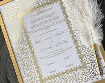 May include: A framed marriage certificate with gold accents and ornate patterns. The certificate includes names and dates, with a decorative feather pen resting on the frame. The frame is gold, and the background is a neutral gray.