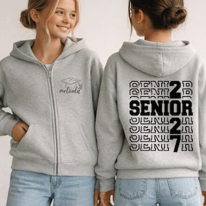 May include: A light gray zip-up hoodie featuring a graduation cap icon and the name Melinda on the front left chest. The back displays the text SENIOR 2027 in a stacked, bold black font with a repeating outline effect for the word SENIOR.
