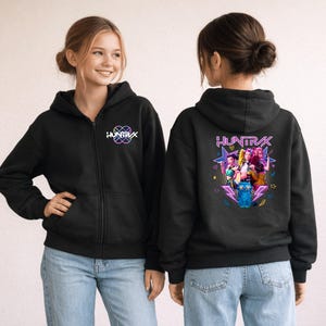 May include: A black zip-up hoodie featuring the text "HUNTRAX" on the left chest. The back displays a vibrant graphic with the text "HUNTRAX" above an illustration of three figures, a blue cat, stars, and lightning bolts in neon pink and blue colors.