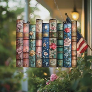 May include: A stained glass window panel in the shape of a stack of books, featuring floral designs. The panel is composed of rectangular sections with images of roses and other flowers in shades of pink, blue, and green. It hangs from a chain.