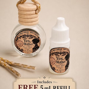 May include: A clear glass car diffuser bottle with a wooden cap and hanging rope, alongside a 5 mL refill bottle. Both feature labels reading The Mad Candler South Carolina, Yes, Mother, Because Mother knows best. A sign states Includes FREE 5 mL REFILL with Every Car Diffuser.