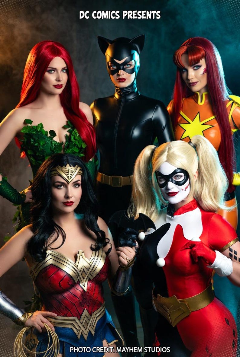 May include: A group of cosplayers dressed as DC Comics characters, including Poison Ivy, Catwoman, Wonder Woman, Harley Quinn, and a character in an orange and yellow costume. The image has the text "DC COMICS PRESENTS" at the top and "PHOTO CREDIT: MAYHEM STUDIOS" at the bottom.