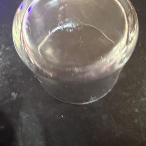 Puede incluir: Un vaso transparente, cil&iacute;ndrico, con base redondeada. El vaso est&aacute; vac&iacute;o y parece limpio. La imagen est&aacute; tomada desde un &aacute;ngulo ligeramente elevado, mirando hacia el interior del vaso. El vaso est&aacute; sobre una superficie oscura.