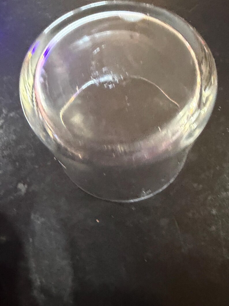 Puede incluir: Un vaso transparente, cil&iacute;ndrico, con base redondeada. El vaso est&aacute; vac&iacute;o y parece limpio. La imagen est&aacute; tomada desde un &aacute;ngulo ligeramente elevado, mirando hacia el interior del vaso. El vaso est&aacute; sobre una superficie oscura.