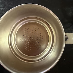 Puede incluir: Un colador de t&eacute; de acero inoxidable con un centro perforado y un asa. El colador tiene forma circular con un borde ligeramente elevado y una serie de peque&ntilde;os agujeros en el centro para filtrar las hojas de t&eacute;.