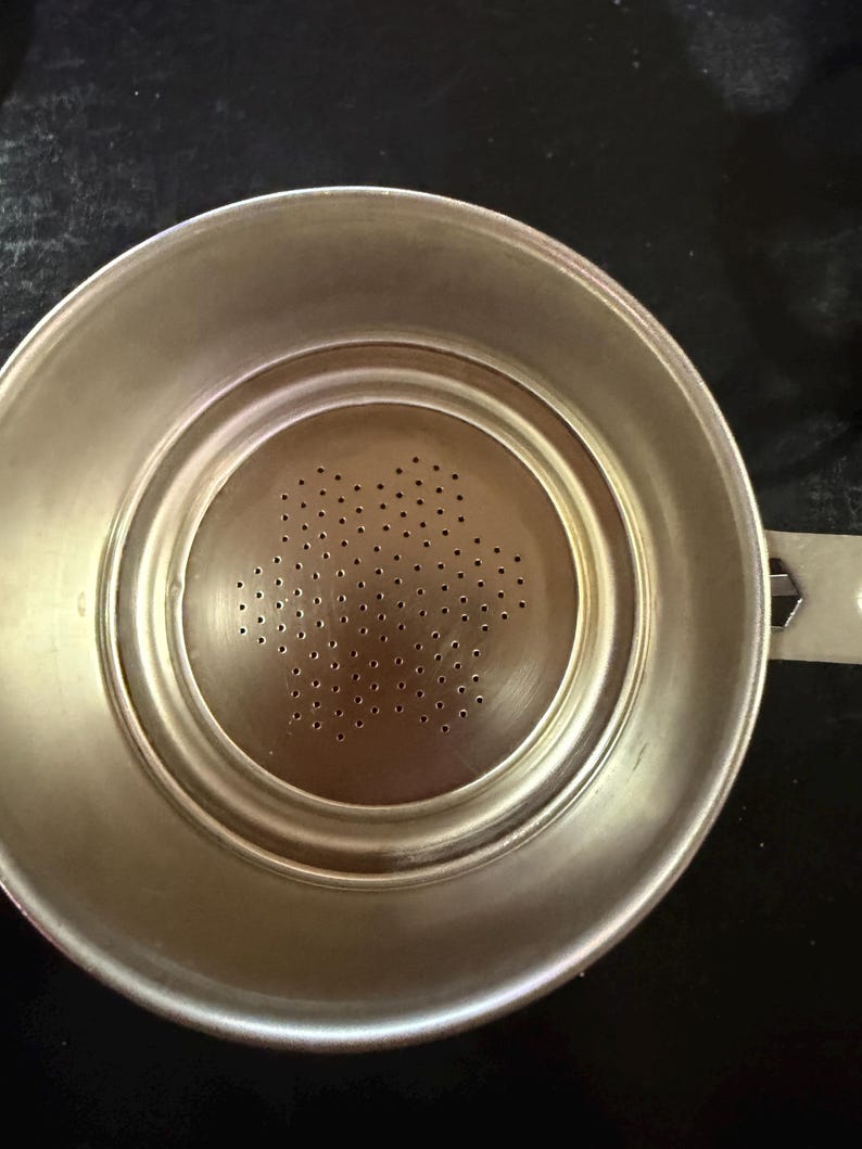 Puede incluir: Un colador de t&eacute; de acero inoxidable con un centro perforado y un asa. El colador tiene forma circular con un borde ligeramente elevado y una serie de peque&ntilde;os agujeros en el centro para filtrar las hojas de t&eacute;.