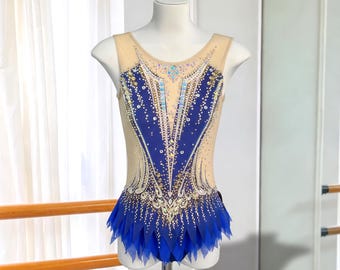 May include: A sleeveless leotard featuring a nude mesh bodice with a deep blue fabric overlay. The garment is heavily embellished with clear and blue crystals arranged in intricate patterns, and the skirt consists of layered blue mesh petals.
