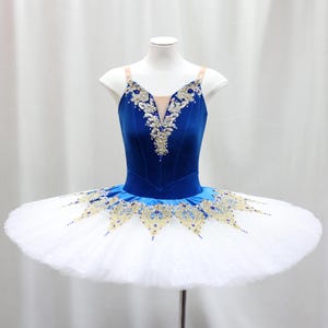 May include: A blue and white ballet tutu with gold and crystal embellishments. The bodice is a deep blue velvet with a V-neck and intricate gold detailing. The skirt is a full, layered white tulle, perfect for dance performances.