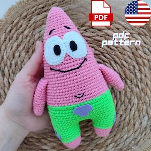 May include: A handmade pink crochet Patrick Star plushie with white eyes and a black smile. The plushie wears green shorts with a purple patch. The image includes a PDF icon and the text "pdf pattern".
