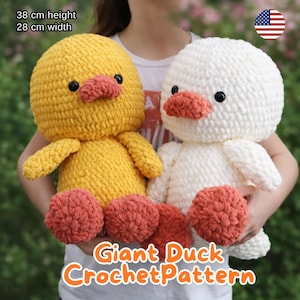 May include: Two large crochet duck toys, one yellow and one white, are held up. The yellow duck is 38 cm tall and 28 cm wide. Both ducks have orange beaks and feet, and black eyes. The text "Giant Duck Crochet Pattern" is at the bottom.