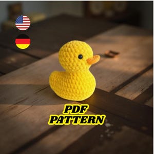 May include: A handmade yellow crochet duck with an orange beak and a black eye. The duck is sitting on a wooden surface. The text "PDF PATTERN" is displayed in yellow and black.