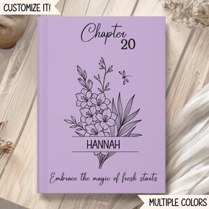May include: A light purple hardcover journal featuring the text Chapter 20, the name HANNAH, and the phrase Embrace the magic of fresh starts. The cover includes a black line art illustration of a floral bouquet with a small dragonfly.