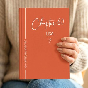 May include: A burnt orange hardcover book featuring white text that reads Chapter 60, LISA, and a small heart icon. The left side includes a vertical white line and the text NEW CHAPTER, NEW ADVENTURE printed in a clean, sans-serif font.
