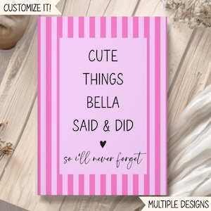 Op de afbeelding: Een rechthoekig notitieboek met een lichtroze middenpaneel en verticale felroze en lichtroze strepen op de randen. De tekst luidt: CUTE THINGS BELLA SAID & DID, gevolgd door een klein zwart hartje en de cursieve tekst: so i'll never forget.