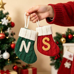 May include: Two small knitted Christmas stockings with white ribbed cuffs and hanging loops. One stocking is dark green with a white letter N, and the other is red with a yellow letter S. Both feature a cable knit texture on the main body.