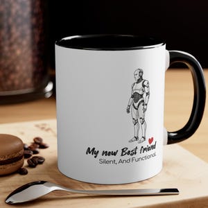 以下が含まれることがあります： 黒い内側とハンドルが付いた白いセラミックマグ。マグには、ロボットの白黒イラストと、赤いハートが付いた「My new Best Friend, Silent, And Functional」というテキストが描かれています。