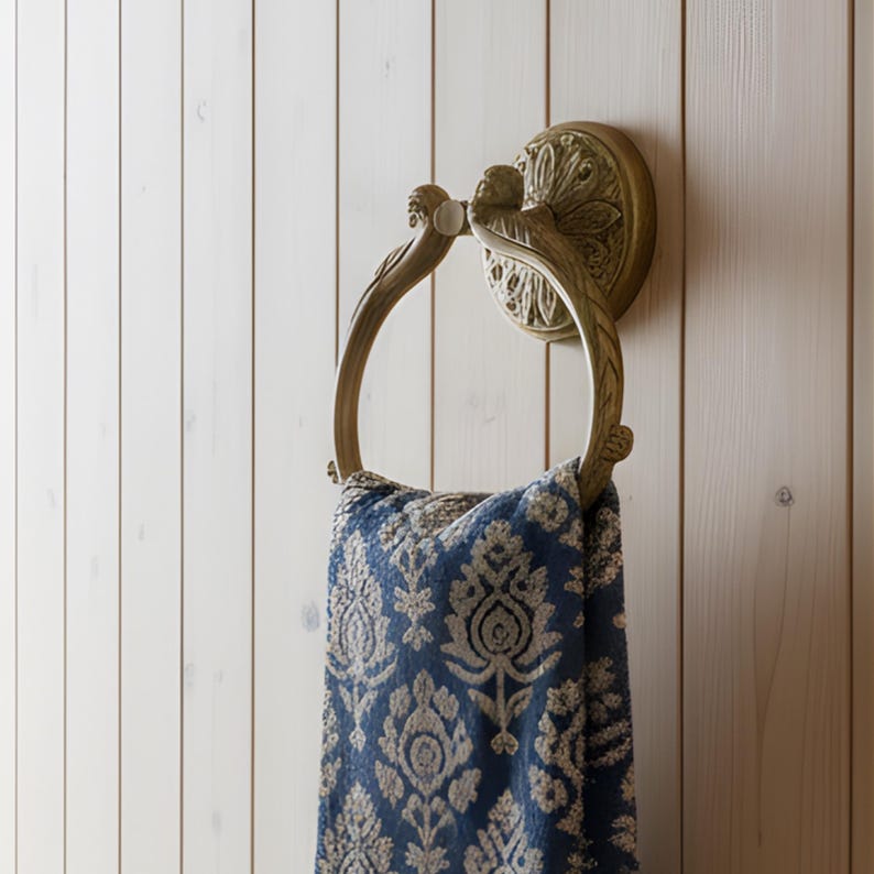May include: A decorative brass towel ring with a floral design, mounted on a white wooden wall. A blue and white patterned towel hangs from the ring, adding a touch of elegance to the bathroom decor.