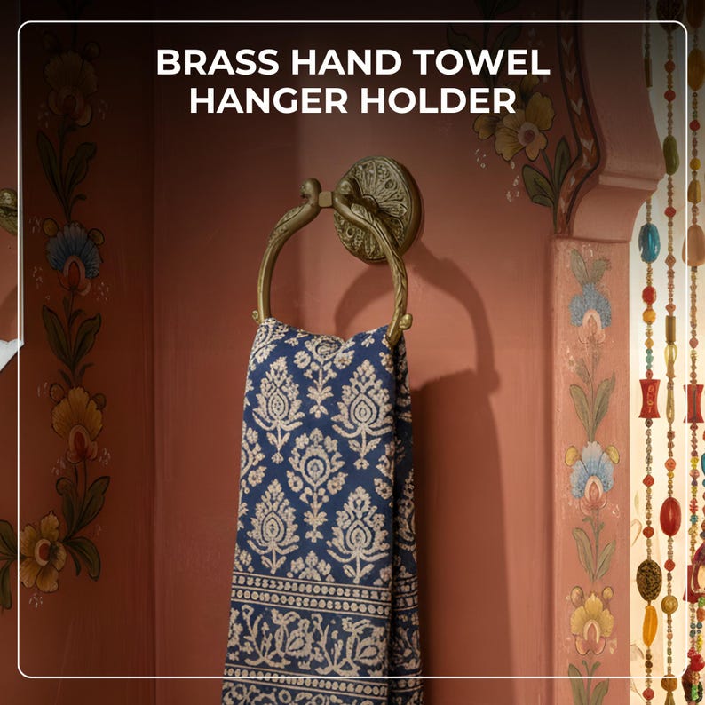 May include: A brass hand towel hanger holder with a decorative ring, holding a blue and white patterned towel. The text "BRASS HAND TOWEL HANGER HOLDER" is at the top of the image. The wall is painted a reddish-orange color.