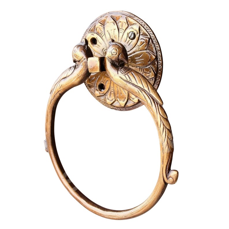 May include: A brass towel ring with a decorative floral backplate. Two bird figures are perched on the ring, which is attached to the backplate. The ring is a warm gold color.