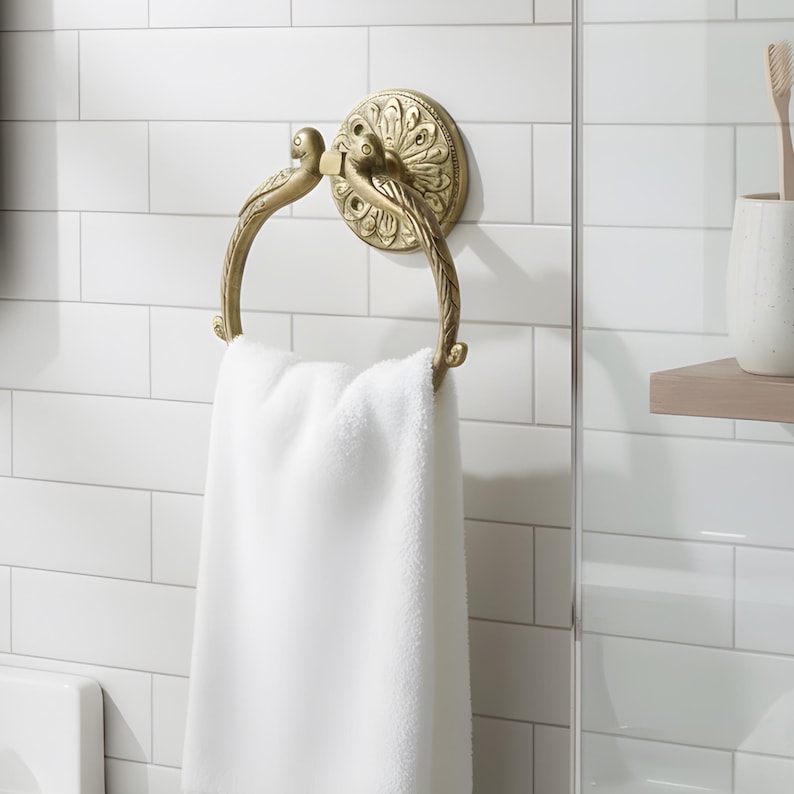 May include: A gold-colored towel ring with a decorative design, holding a white towel. The ring is mounted on a white tiled wall, adding a touch of elegance to the bathroom.