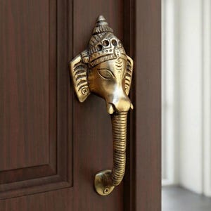 May include: A brass elephant-shaped door handle, featuring intricate details on the head and trunk. The handle is mounted on a dark brown wooden door, showcasing a decorative and functional design. The handle's dimensions are approximately 8 inches in length.