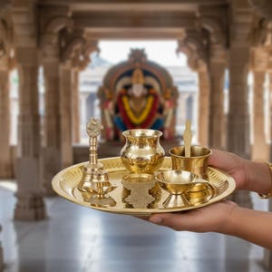 May include: A golden brass puja thali, or offering plate, holds various ritual items. The thali includes a small bell, a water pot, a cup with a spoon, a small bowl, and a decorative stand. The items are arranged on a round, golden plate.