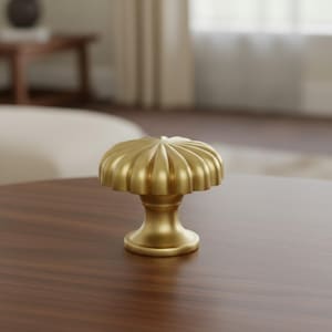 Pode incluir: Um puxador de armário dourado com um design canelado em forma de cogumelo. O puxador está sobre uma superfície de madeira castanha escura. O puxador tem uma base redonda e um topo decorativo, adequado para ferragens de móveis.