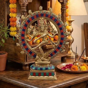 Könnte beinhalten: Eine Messingstatue einer tanzenden Gottheit, umrahmt von einem kreisförmigen Design mit roten und blauen Akzenten. Die Statue steht auf einem dekorativen Sockel mit türkisen und roten Details. Religiöses oder spirituelles Thema.