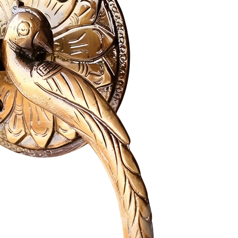 May include: A detailed, gold-colored metal bird-shaped door handle. The handle features a bird perched on a decorative circular base with intricate floral and leaf patterns. The bird's feathers and beak are clearly defined.
