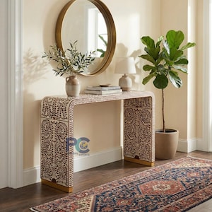 May include: A rectangular console table with a curved waterfall edge design, featuring an intricate brown and cream floral inlay pattern. The table has a solid base and is positioned against a wall, topped with a ceramic vase and books.