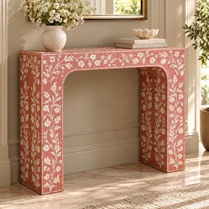Pode incluir: Uma mesa consola retangular com acabamento em rosa antigo e incrustações brancas de videiras florais. A mesa possui um tampo liso e dois painéis laterais verticais com cantos internos arredondados, exibindo um padrão botânico contínuo.