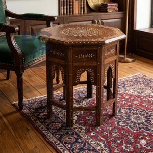 May include: An octagonal wooden side table featuring intricate light-colored floral and geometric inlay patterns on the top and sides. The table stands on six legs with arched cutouts and is decorated with small, evenly spaced inlaid dots.