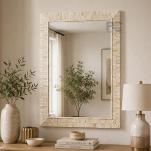May include: A rectangular wall mirror featuring a frame constructed from small, light-colored, rectangular tiles arranged in a brick-like pattern. The mirror reflects a room with a window, a potted plant, and a framed picture on the wall.