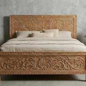 Puede incluir: Una cama de madera tallada con intrincados diseños florales. El cabecero y el piecero presentan detallados patrones de hojas y vides. La cama es de madera marrón claro y está rodeada de plantas en macetas.