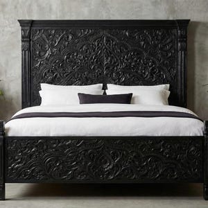 Puede incluir: Una cama de madera negra tallada intrincadamente con una cabecera a juego. La cama está hecha con ropa de cama blanca y una almohada y un camino de cama negros. Plantas en macetas en macetas de terracota flanquean la cama.