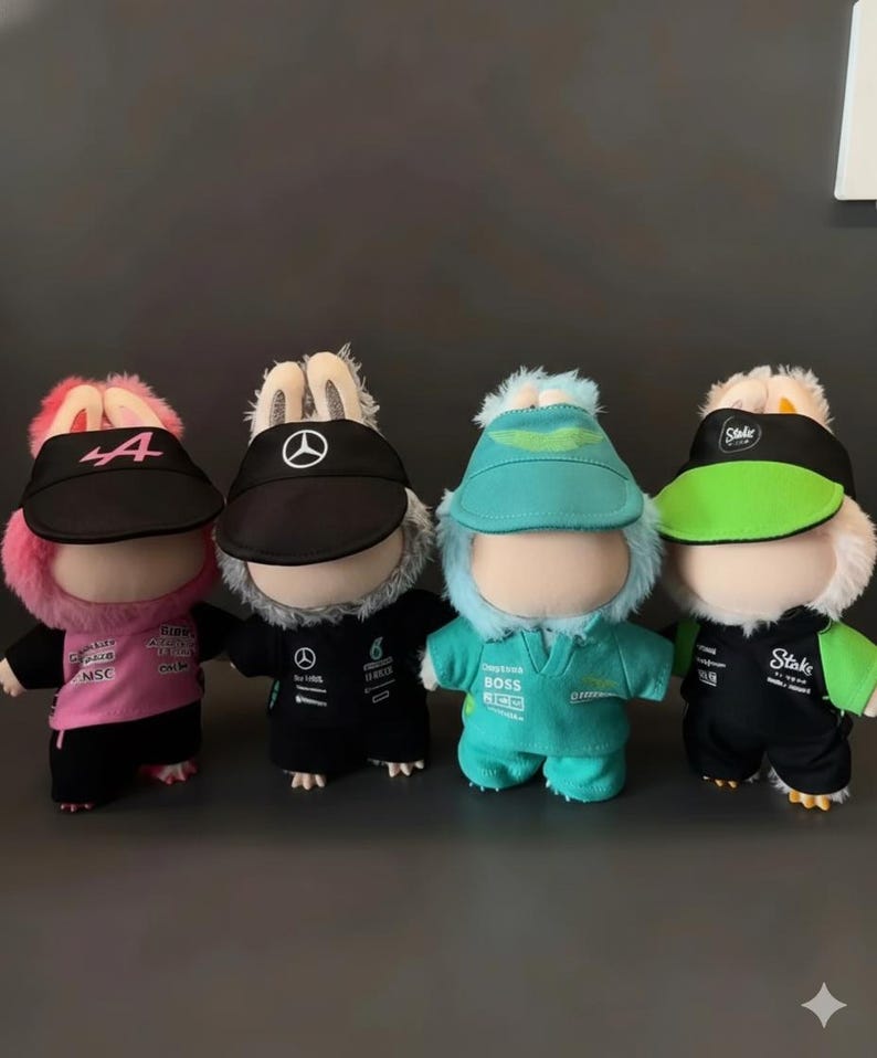 May include: Four plush dolls wearing racing team uniforms and visors. The dolls have bunny ears and are dressed in pink, black, teal, and green outfits. Each visor displays a team logo or number.