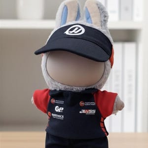 May include: A plush rabbit doll wearing a black visor with a white logo, a black and red uniform, and black shorts. The uniform has the text "GP BARENICE" and "AWSS". The doll is standing on a wooden surface.