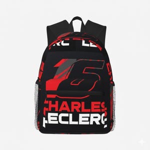 Peut inclure: Sac à dos noir avec le nom "CHARLES LECLERC" en blanc et rouge, et le numéro 16 en rouge et gris. Il possède une poche latérale en filet et une poignée supérieure.