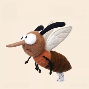 Op de afbeelding: Een pluche mug met een bruin lichaam, oranje achterlijf en witte vleugels. Het speelgoed heeft grote witte ogen, een lange bruine snuit en zwarte poten en antennes. De mug lijkt te vliegen.