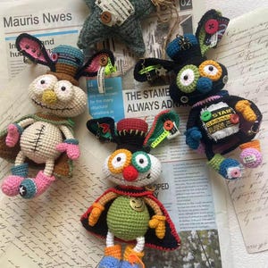 May include: A selection of handmade crochet dolls and a star-shaped ornament. The dolls have whimsical designs with colourful details, including button accents, and are set against vintage paper. The star is green.