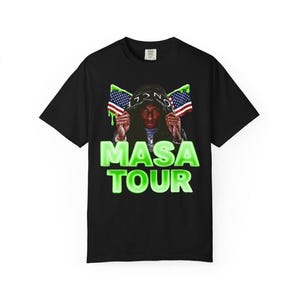 Pode incluir: Camiseta preta com um gr&aacute;fico de uma pessoa usando um capuz segurando bandeiras americanas. O texto "MASA TOUR" &eacute; exibido em verde neon abaixo.