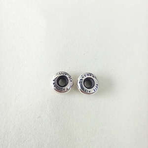 May include: Two circular silver charms with a polished finish. Each charm features a dark center hole and is engraved with the text PANDORA and 925 ALE along the outer rim. These small metal components are designed for jewelry assembly and customization.