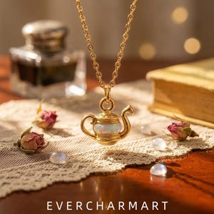 Könnte beinhalten: Eine goldfarbene Halskette mit einem teekannenförmigen Anhänger, der in der Mitte einen schillernden Opal aufweist. Der Anhänger hängt an einer zarten Goldkette. Der Text EVERCHARMART steht unten im Bild in einer weißen serifenlosen Schrift.