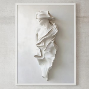 Puede incluir: Escultura de pared blanca enmarcada de una figura drapeada. La obra de arte es un relieve, con detalles de tela fluida. La escultura cuelga sobre una cama con ropa de cama blanca y un cabecero de madera.