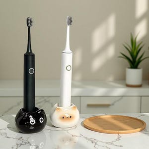 May include: Two electric toothbrushes, one black and one white, are displayed in decorative holders. The black toothbrush is in a glossy black holder with a cat face design. The white toothbrush is in a cream-colored holder with a cat face. A wooden tray sits nearby.